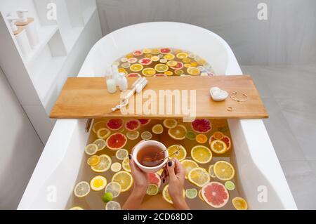 Gesichtslose Frau in der Badewanne mit Scheiben von Orangen, Zitrone und Grapefruits liest das Buch. Frau mit Detox Bad Behandlung. Pediküre-Tools ein Stockfoto