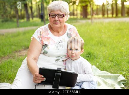 Ältere Frau mit Enkelkind entspannen Sie sich in der Natur und mit modernen Notebook Stockfoto