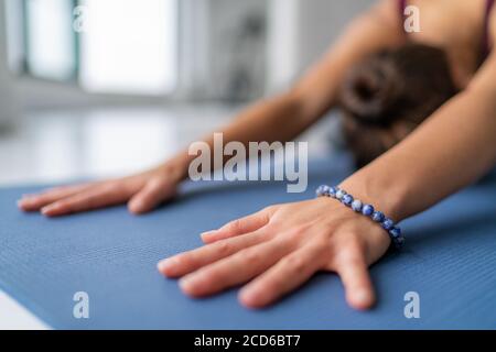 Yoga Meditation Frau tut Kinder Pose Stretching im Fitnessstudio oder Wohnzimmer zu Hause. Nahaufnahme der Hände berühren Boden Trainingsmatte und Armband Stockfoto