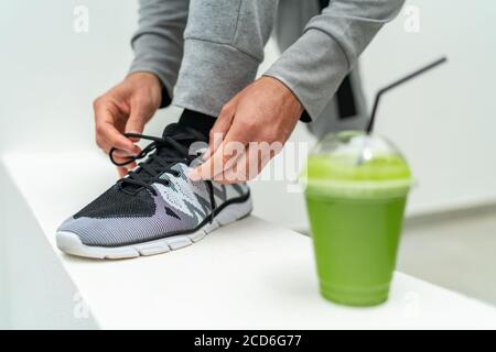 Smoothie Juice Drink Fitness-Mann Schnürung Laufschuhe, Athlete Läufer mit grünem Gemüse Detox Saft immer bereit für den morgendlichen Lauf binden Schnürsenkel an Stockfoto