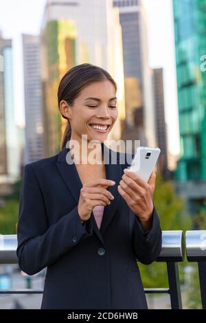 Frau mit Telefon - asiatische Geschäftsfrau hält Smartphone SMS auf Messenger-App online an Geschäftsleute. Arbeiten draußen zu Fuß in der Stadt Straße Stockfoto