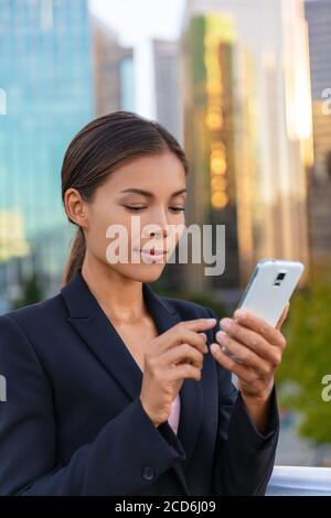 Asiatische Geschäftsfrau SMS auf Handy Blick auf Online-Banking bei der Arbeit. Bürogebäude Stadtmenschen in Anzug. Chinesische Geschäftsfrau mit Stockfoto