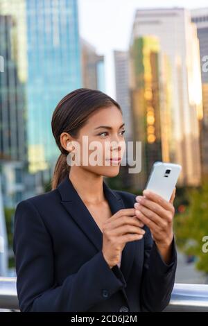 Asiatische Geschäftsfrau SMS auf Handy Blick weg auf die Seite Stadt Hintergrund. Bürogebäude im Freien Arbeitsleute. Chinesische Geschäftsfrau Stockfoto
