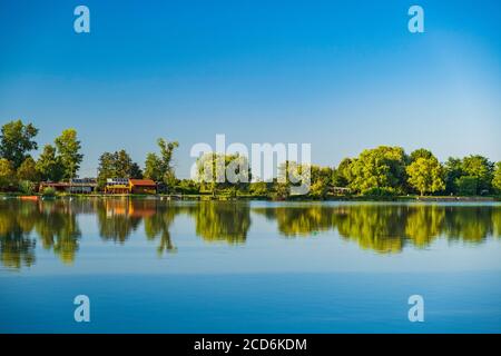 Blockhütten und Ferienhäuser unter Bäumen am See in Varazdin, ländliches Kroatien Stockfoto