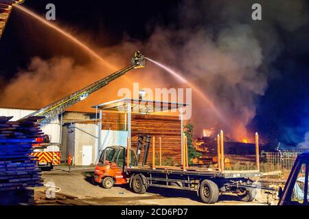 Limburg, Deutschland. August 2020. Feuerwehrleute löschen ein Feuer in einem Sägewerk in Elz bei Limburg. Während der Löscharbeiten wurde eine regionale Eisenbahnlinie geschlossen, um Leitungen für Löschwasser über die Schienen zu verlegen. Die Schließung sollte bis etwa 10 Uhr dauern, sagte eine Sprecherin der Hessischen Staatsbahn. Betroffen waren die Linien RB29 und RB90, und von Limburg aus wurde ein Ersatzdienst eingerichtet. Bundesstraße 8 war ebenfalls vorübergehend gesperrt. Diese Blockade könnte jedoch am frühen Donnerstagmorgen wieder aufgehoben werden. Quelle: Maximilian See/dpa/Alamy Live News Stockfoto