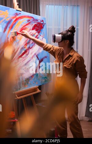 Painter mit Virtual Reality-Headset und die Schaffung eines Meisterwerks auf großer Leinwand. Moderne Kunst malen auf Leinwand, kreative, zeitgenössische und erfolgreiche bildende Kunst Künstler Zeichnung Meisterwerk Stockfoto