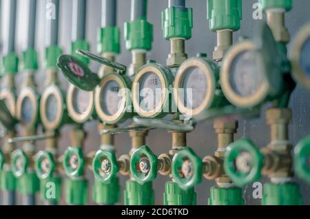 Reihe von Industrierohrleitungen und Armaturen mit grünen Rädern auf Graue Wand zur Überprüfung des Standardwasserstands in Der Schlafsaal für überprüfen Sie den Preis Stockfoto