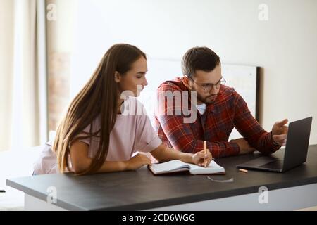 Beeindruckende seriöse Mann sitzt in komfortablen Café, Blick auf Laptop-Computer, zeigen mit dem Finger notwendige Informationen, erklärt junge Dame proc Stockfoto