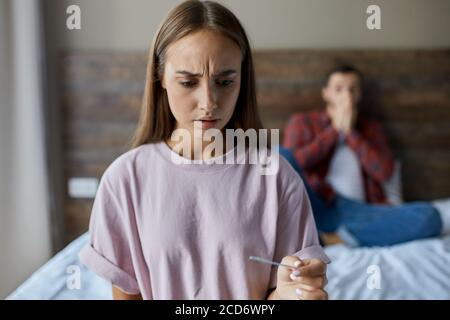 Nahaufnahme von jungen hübschen Mädchen mit langen schönen Haaren, hält in der Hand Schwangerschaft Test, schockiert durch Ergebnisse, Blick weg mit Angst, weiß nicht, was t Stockfoto