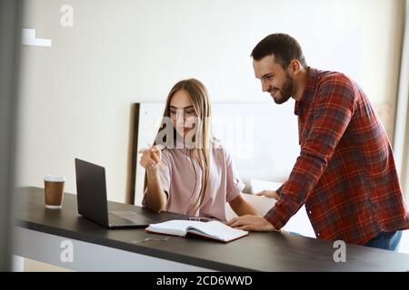 Attraktive große Mann mit dicken stilvollen Bart glücklich schaut auf Computer-Bildschirm, chattet mit charmanten Mädchen optimistisch, hält Palm auf schwarzem Tisch, fam Stockfoto