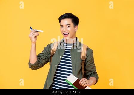 Fun travel Concept Portrait von lächelnden jungen männlichen asiatischen Touristen Halten von Flugzeugspielzeug mit Pass und Ticket in isoliertem Studio Gelber Hintergrund Stockfoto