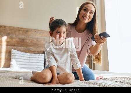 Nahaufnahme von charmanten aufgeregt Frau mit Zapper in den Händen, Blick weg mit positiven Emotionen, glücklich lächeln, die Wahl lustige Cartoons für kleine Beau Stockfoto