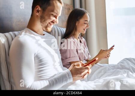 Positive Atmosphäre, samstagmorgen, Sonne scheint hell, junge Menschen ignorieren Live-Kommunikation und Blick auf Handy-Bildschirme, zum Ausdruck Happ Stockfoto
