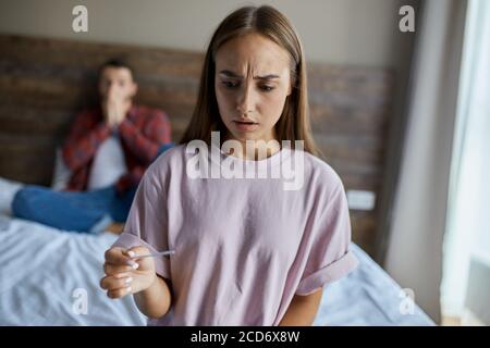 Schließen Sie Foto von verärgert Mädchen im Schlafzimmer stehen, halten Schwangerschaftstest, Blick weg mit schockierten Ausdruck, unzufrieden durch Ergebnis, kann h nicht glauben Stockfoto