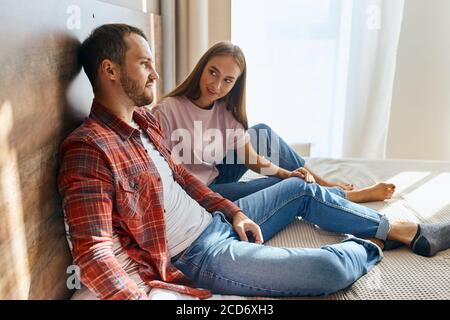 Nahansicht der charmanten Dame und brutal gut aussehenden Mann auf weichem Bett ruhen, miteinander reden, wegschauen mit positiven Emotionen, hübsche Freundin Stockfoto