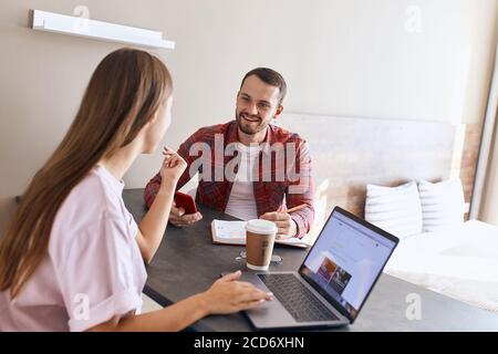 Schönes junges Paar im hellen Schlafzimmer reden, sitzen am dunklen Tisch, diskutieren täglichen Routinearbeit, mit Geräten, Familienkonzept Stockfoto