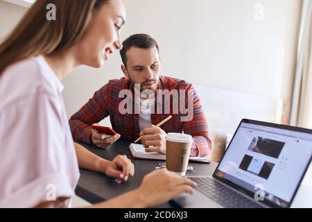 Happy Loving Paar sitzt vor dem Computer, auf der Suche nach einem Ort, um am Wochenende zu gehen, nachdenkliche Mann hält Stift, bereit, Notizen zu machen, aus der Nähe, Zeit ein Stockfoto