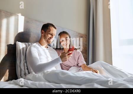 Portrait von schönen unrasiert Mann halten rote Handy, laufen durch Fotos zusammen mit beautifeul Frau, Blick auf den Bildschirm, Konzept über die Liebe Stockfoto