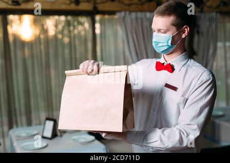 Lieferung von Essen aus dem Restaurant. Porträt eines Kellners, der eine Bastelpapiertasche für die Lieferung von Lebensmitteln hält. Stockfoto