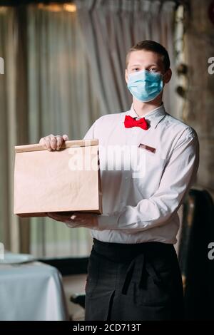 Lieferung von Essen aus dem Restaurant. Porträt eines Kellners, der eine Bastelpapiertasche für die Lieferung von Lebensmitteln hält. Stockfoto