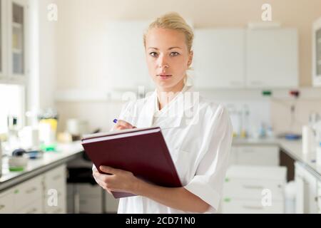 Porträt von jungen, selbstbewussten weiblichen Gesundheitsfachkraft Notizen während der Inventur im wissenschaftlichen Labor oder Arztpraxis Stockfoto
