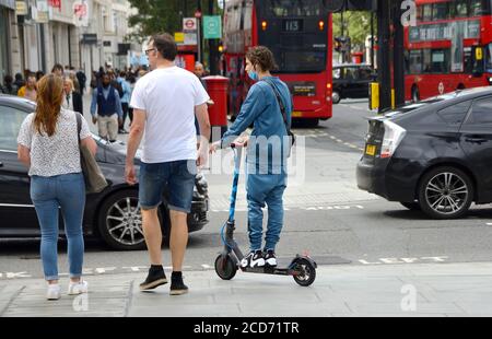 London, England, Großbritannien. Junger Mann auf einem Elektroroller an einem Fußgängerübergang auf dem Bürgersteig in der Oxford Street Stockfoto