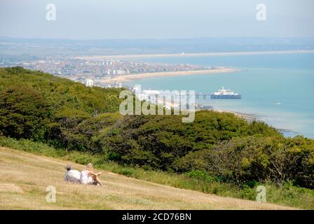 Zwei Leute sitzen auf dem Gras und blicken in Richtung Eastbourne in der Ferne von Beachy Head, East Sussex, England Stockfoto