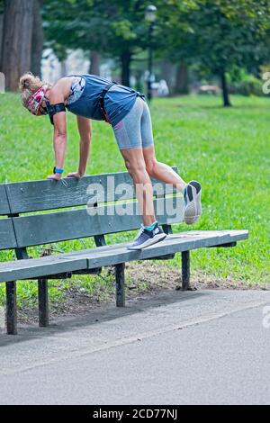 Eine fitt Frau mittleren Alters streckt ihre Calk Muskeln auf einer Bank. In einem Park in Flushing, Queens, New York City. Stockfoto