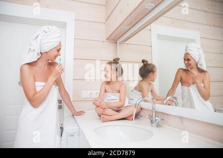 Glückliche liebevolle Familie Zähneputzen und verbringen Zeit zusammen. Mutter und ihre Tochter Kind Mädchen küssen und umarmen in weißen Badezimmer. Frau und Stockfoto