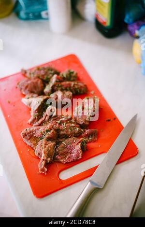 Rohes, geschnittenes Steak auf einem roten Schneidebrett mit einem großen Messer. Stockfoto