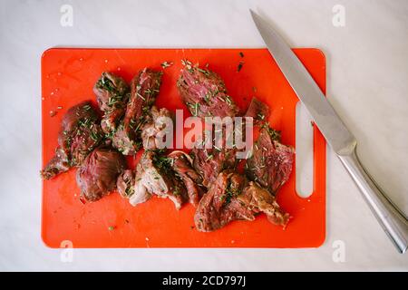 Rohes, geschnittenes Steak auf einem roten Schneidebrett mit einem großen Messer. Stockfoto