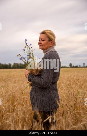 Eine ältere Frau von 65 Jahren steht in einem Roggenfeld. Stockfoto
