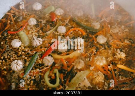 Nahaufnahme der Textur des zubereitenden usbekischen Pilafs - kochendes Wasser mit Karotten, Paprika, Knoblauch und Kichererbsen. Zusatz von Gewürzen, Berberitze und duftend Stockfoto