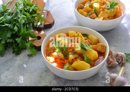Gemüseeintopf in einer weißen Schüssel. Heller Hintergrund. Leinenstoff. Mit Kartoffeln, Huhn, Karotten und Kräutern einkochen. Stockfoto