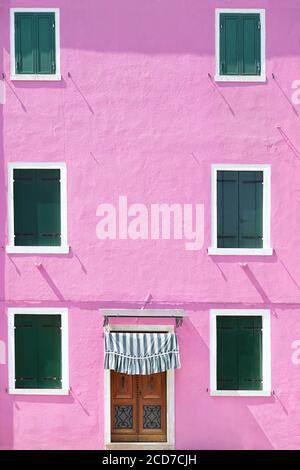 Pink bemalte Wand mit mehreren Fenstern mit grünen hölzernen Fensterläden, auf der Insel Burano, Venedig, Italien Stockfoto