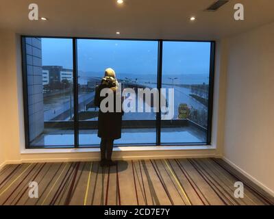 Frau steht an einem regnerischen Tag in Dundee vor einem großen Fenster Stockfoto