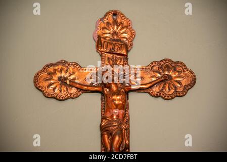 Bild eines alten Kruzifixes, das an der Mauerwerkswand aus verzinktem Eisen hängt und künstlich gealtert ist. Religiöses Artefakt. Symbol der katholischen Kirche Stockfoto