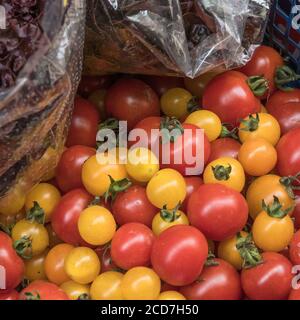 Kleine rote und gelbe Kirschtomaten zum Verkauf in einem Supermarkt an der Ecke. Aus der Rebe selbst angebaute Kirschtomaten. Lebensmittel ohne Kunststoffverpackung. Stockfoto