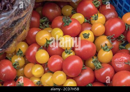 Kleine rote und gelbe Kirschtomaten zum Verkauf in einem Supermarkt an der Ecke. Aus der Rebe selbst angebaute Kirschtomaten. Lebensmittel ohne Kunststoffverpackung. Stockfoto