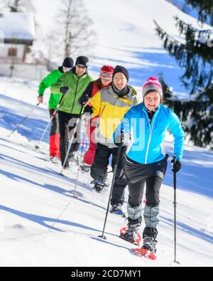 Eine Gruppe von gut gelaunten Menschen, die sich einem Schneeschuh Wanderung in der winterlichen Natur an einem kalten, sonnigen Tag Stockfoto