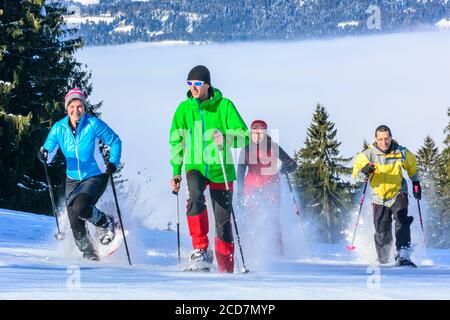 Eine Gruppe von gut gelaunten Menschen, die sich einem Schneeschuh Wanderung in der winterlichen Natur an einem kalten, sonnigen Tag Stockfoto