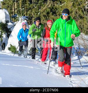 Eine Gruppe von gut gelaunten Menschen, die sich einem Schneeschuh Wanderung in der winterlichen Natur an einem kalten, sonnigen Tag Stockfoto