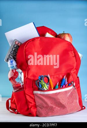 Stilvoller Rucksack mit verschiedenen Schule stationär auf einem weißen Holztisch auf blauem Hintergrund. Stockfoto