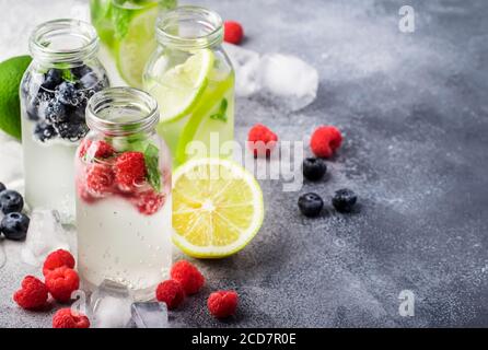 Beerengetränke und Zitrusfrüchte, alkoholfreie Getränke und Cocktails in Glasflaschen auf grauem Steintisch-Hintergrund, Kopierraum Stockfoto