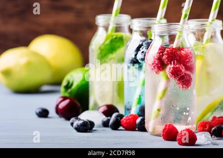 Sommergetränke. Beeren, Früchte und Zitrusfrüchte alkoholfreie erfrischende eiskalte Getränke und Cocktails in Glasflaschen auf blauem Hintergrund Stockfoto