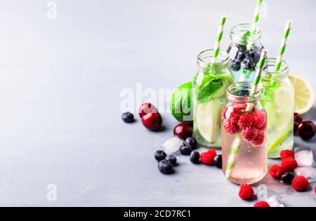 Beeren, Früchte und Zitrusfrüchte alkoholfreie kalte Getränke und Cocktails in Glasflaschen auf blauem Hintergrund, Kopierraum Stockfoto