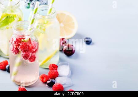 Sommergetränke. Beeren, Früchte und Zitrusfrüchte alkoholfreie erfrischende eiskalte Getränke und Cocktails in Glasflaschen auf blauem Hintergrund Stockfoto