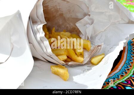 Nahaufnahme von frittierten Chips in weißem Papier verpackt Zum Mitnehmen, um im Sommer draußen zu essen auf Pretty Tischtuch Stockfoto