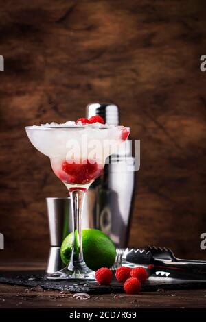 Himbeer-Daiquiri, alkoholischer Cocktail mit weißem Rum, Limettensaft, Himbeeren und zerstoßenem Eis in hohem Glas, auf Holztheke mit Stahlstange Stockfoto
