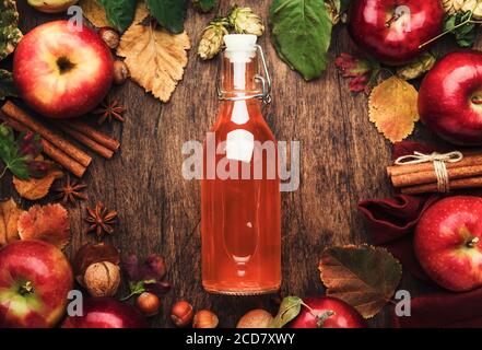 Apfelessig. Flasche frischen Bio-Apfelessig auf Holztischhintergrund mit Zimtstangen, Anisstern, Nüssen und gefallenen Blättern. Gesundheit Stockfoto